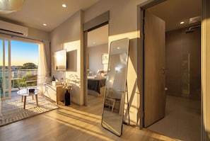 Ein modernes Hotelzimmer mit einem großen Spiegel, einem Flachbildfernseher, einem Balkon mit Aussicht und Holzboden.