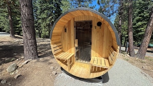 Uma estrutura circular de madeira, parcialmente fechada, com um banco no interior e uma porta para um espaço interno.
