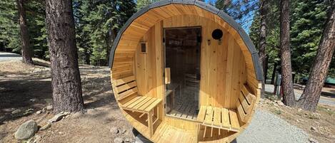 A wooden, circular, semi-enclosed structure with a bench inside and a door leading to an interior space.