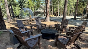 Um camping arborizado com cadeiras Adirondack e uma lareira.