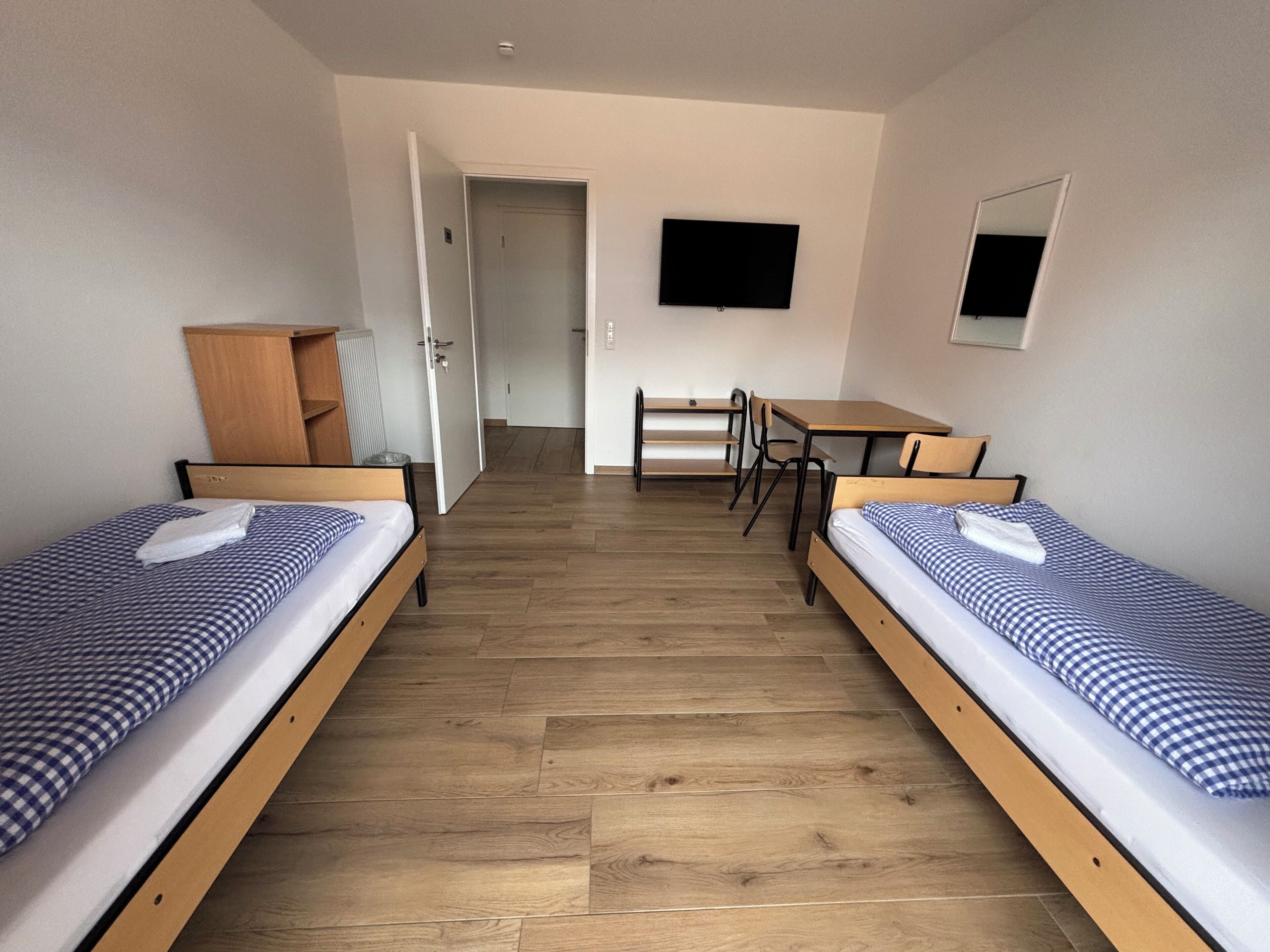 Een hotelkamer met twee éénpersoonsbedden, een bureau, een stoel en een televisie.