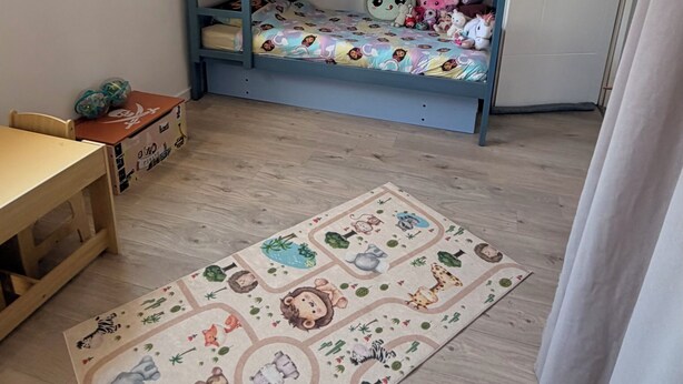 Ein Kinderzimmer mit Etagenbetten, einem Schreibtisch, einer roten Hängelampe und einem Teppich mit Tiermotiven.