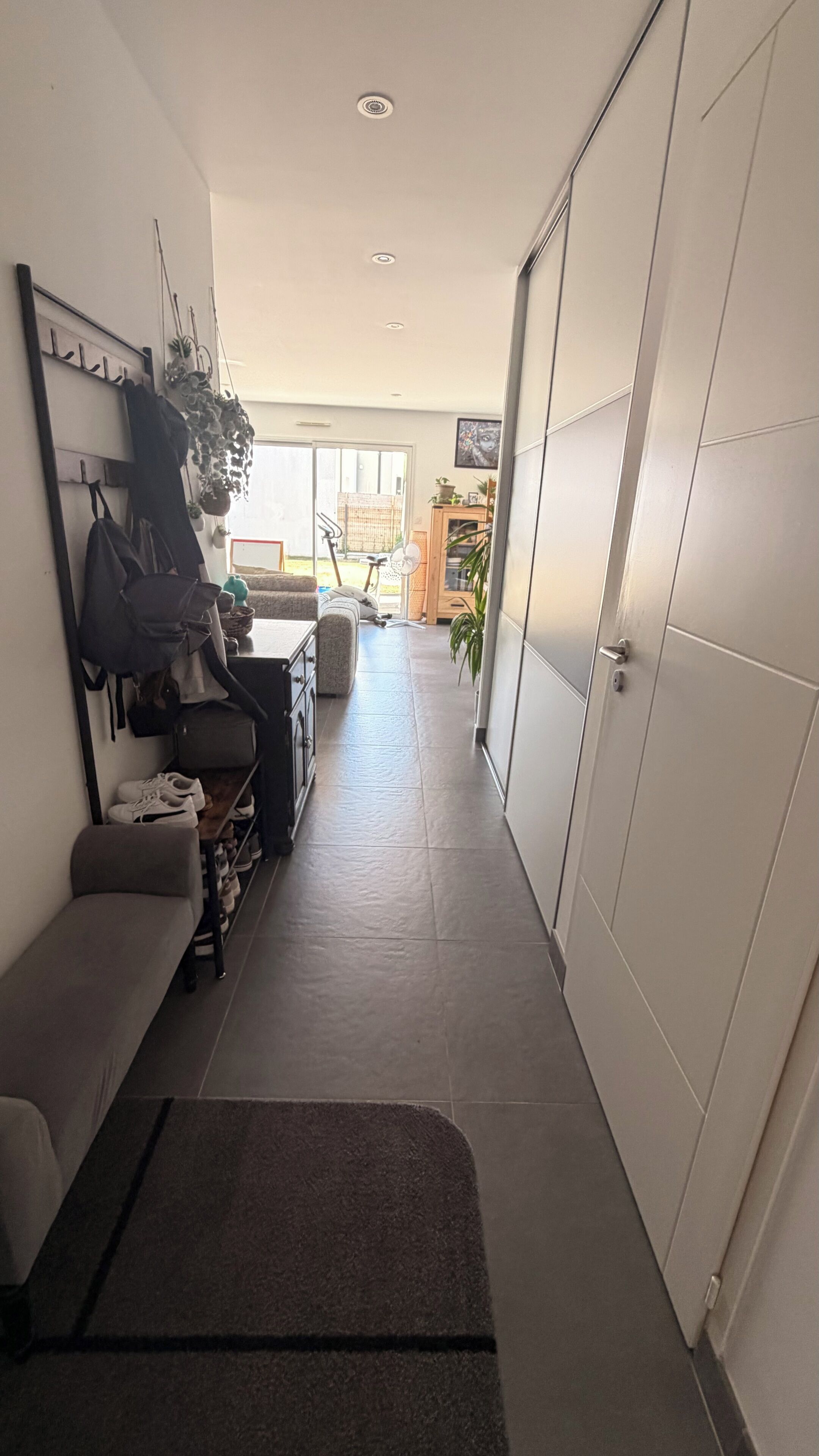 A narrow hallway with a bench, a coat rack, and a sliding door.