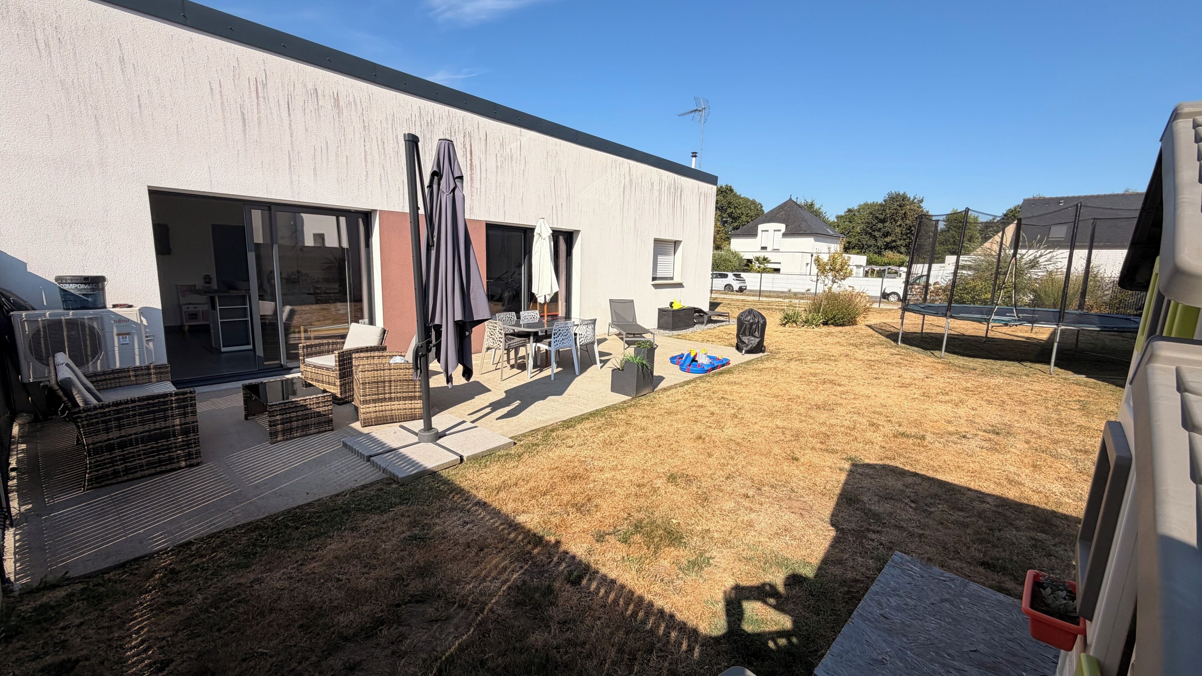 A modern house with a patio, outdoor furniture, and a trampoline.
