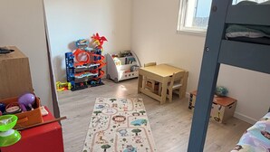 Ein Kinderzimmer mit Etagenbett, einem Holztisch, einem bunten Teppich und einem Spielzeugschrank.