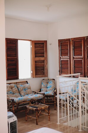 A room with a white ceiling, wooden shutters on the windows, a white railing, and a bamboo chair.