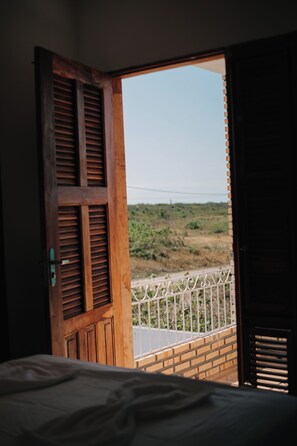 Eine offene Holztür, die auf einen Balkon mit Blick auf eine hügelige Landschaft führt.
