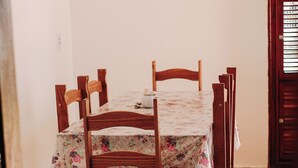 A dining table with six wooden chairs, a floral tablecloth, and a window with blinds. - A cozy, spacious home for families and couples (sleeps 6), just 5 minutes from the beach (Lagoinha Paraipaba)