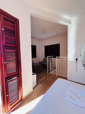 A bedroom with a bed, a wooden door, a staircase, and a seating area with chairs. - A cozy, spacious home for families and couples (sleeps 6), just 5 minutes from the beach (Lagoinha Paraipaba)