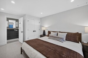 A modern bedroom with a large bed, a nightstand, a bedside table, a wardrobe, and a bathroom with a mirror and sink. - Brand-New Luxury Lodge | 17 Private Acres | 30 Minutes to Yellowstone (Livingston)