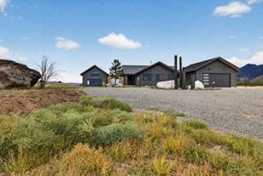 A modern two-story house with a gravel driveway and a large rock in the foreground. - Brand-New Luxury Lodge | 17 Private Acres | 30 Minutes to Yellowstone (Livingston)
