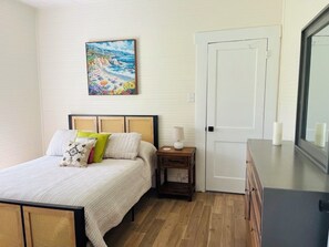 A bedroom with a bed, bedside table, lamp, and a painting on the wall.