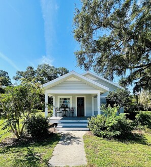 A white house with a porch, two chairs, and a pathway leading to the entrance.