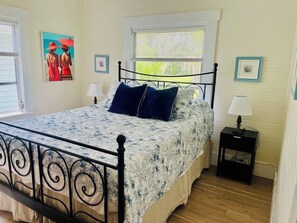A bedroom with a bed, two bedside tables, a window, and wall art.