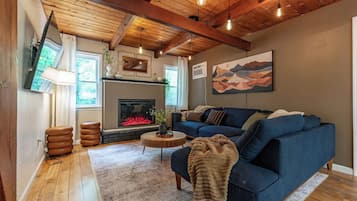 Una sala de estar acogedora con chimenea, un sofá azul y un techo de madera.