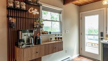 A kitchen with a coffee station, wooden ceiling, and a window overlooking greenery.