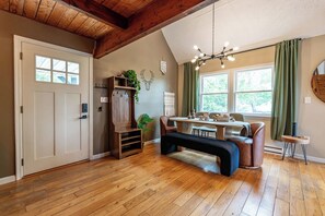 Una habitación con piso de madera, un banco, una mesa con sillas, una lámpara colgante y una puerta con ventana.
