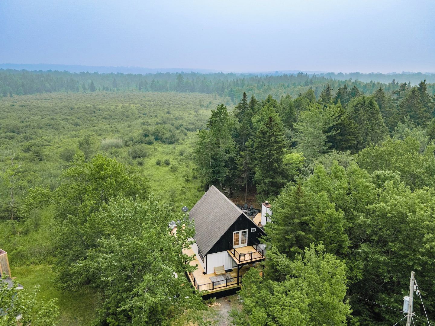 A cabin with a deck, surrounded by dense forest and a clear view of the landscape.