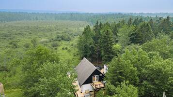 A cabin with a deck, surrounded by dense forest and a clear view of the landscape.