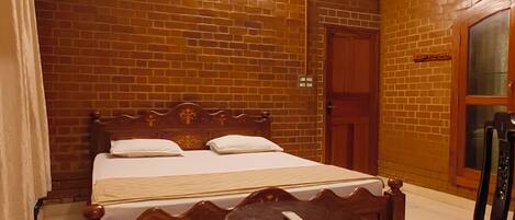 A room with a bed, a chair, a table, a ceiling fan, and a brick wall.
