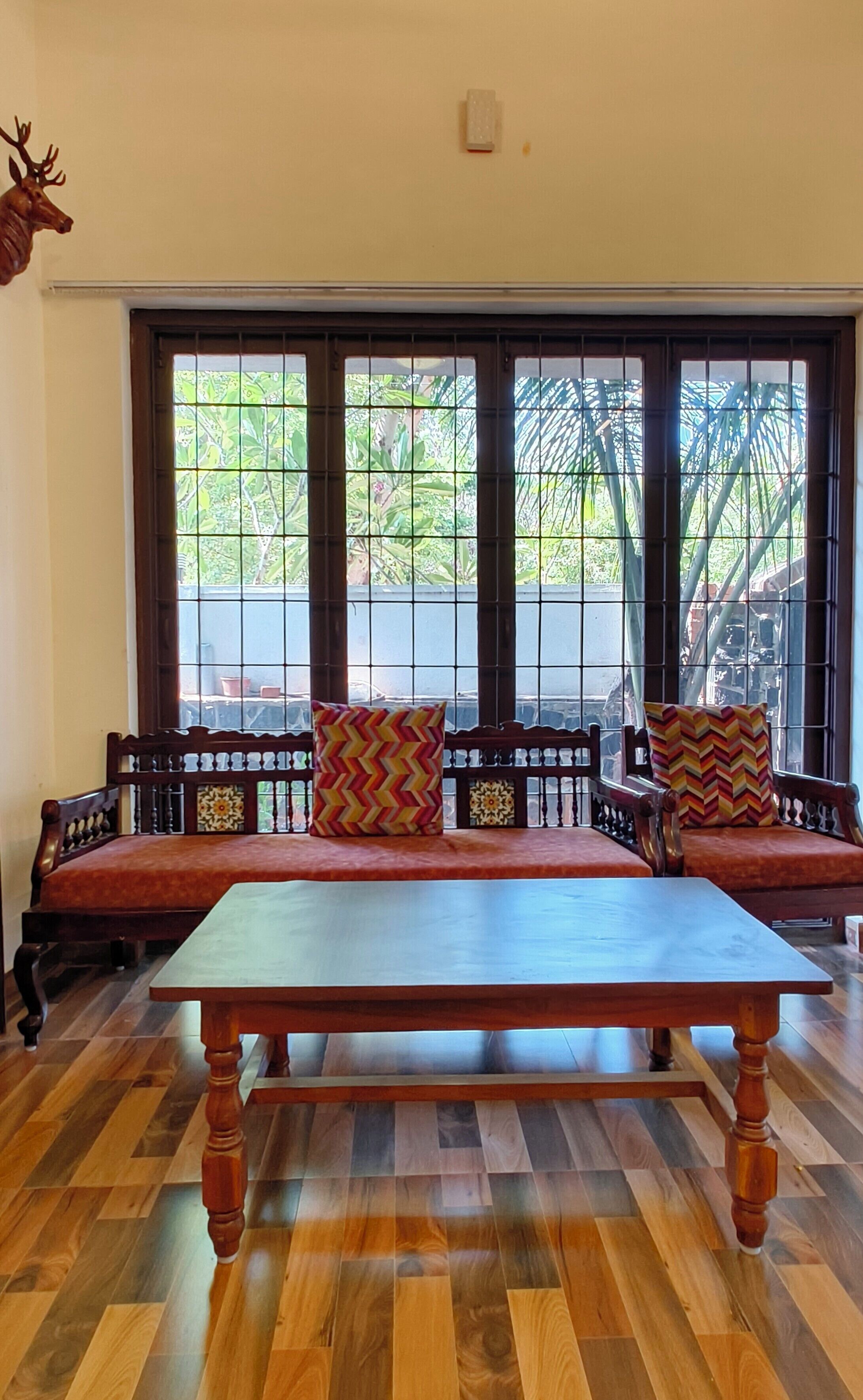 A room with a wooden table and benches, a decorative wall piece, and a window with a view of greenery.