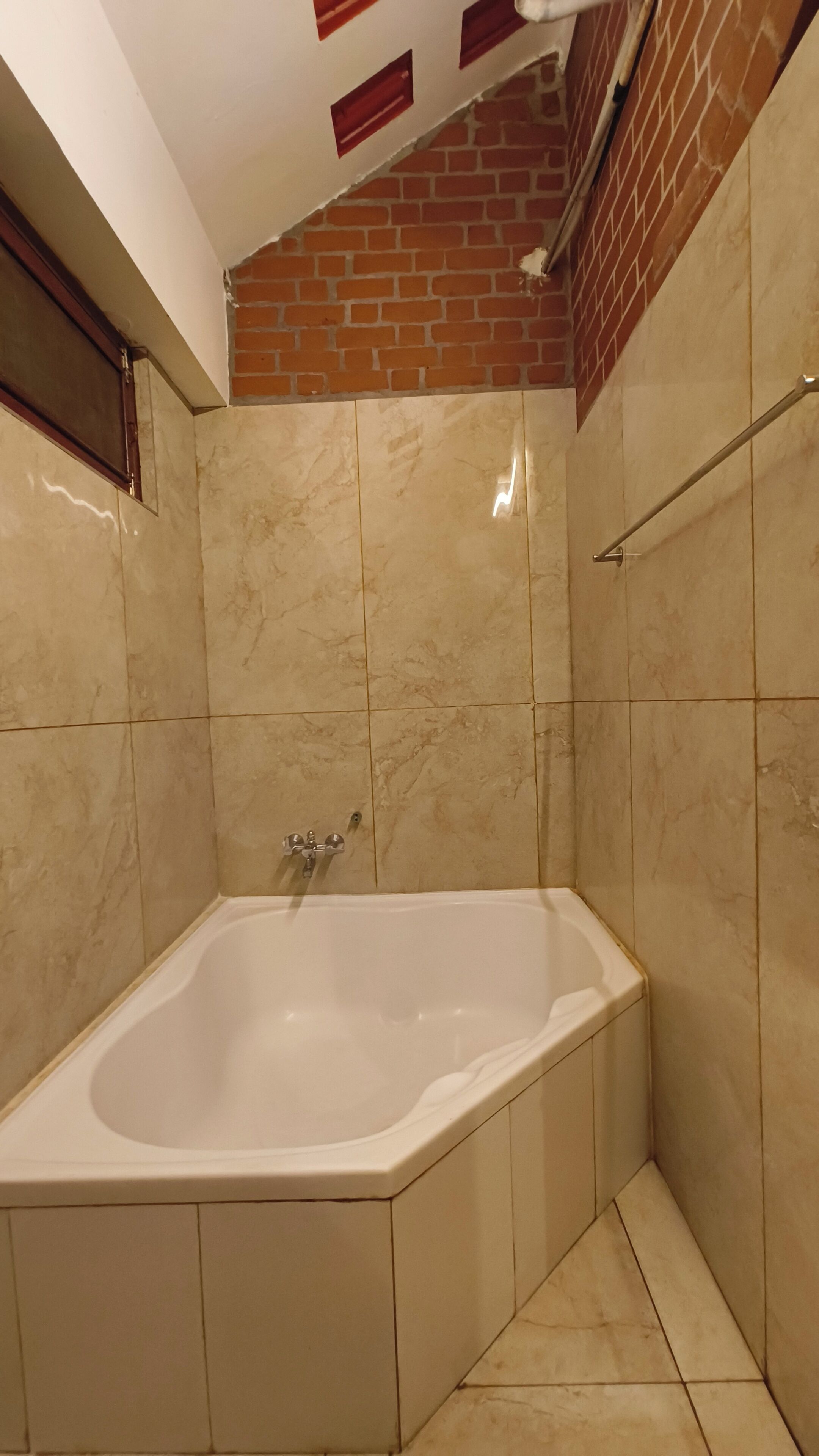 A bathroom with a bathtub, tiled walls, and a visible brick wall section.