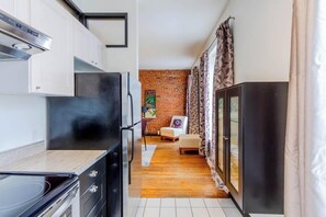 A compact kitchen with modern appliances, a dining area with a brick wall, and a view into a living space. - Appartement du Vieux-Québec (Québec)