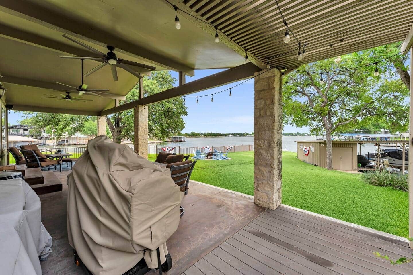 A covered outdoor area with a barbecue grill, seating, and a view of a lake.