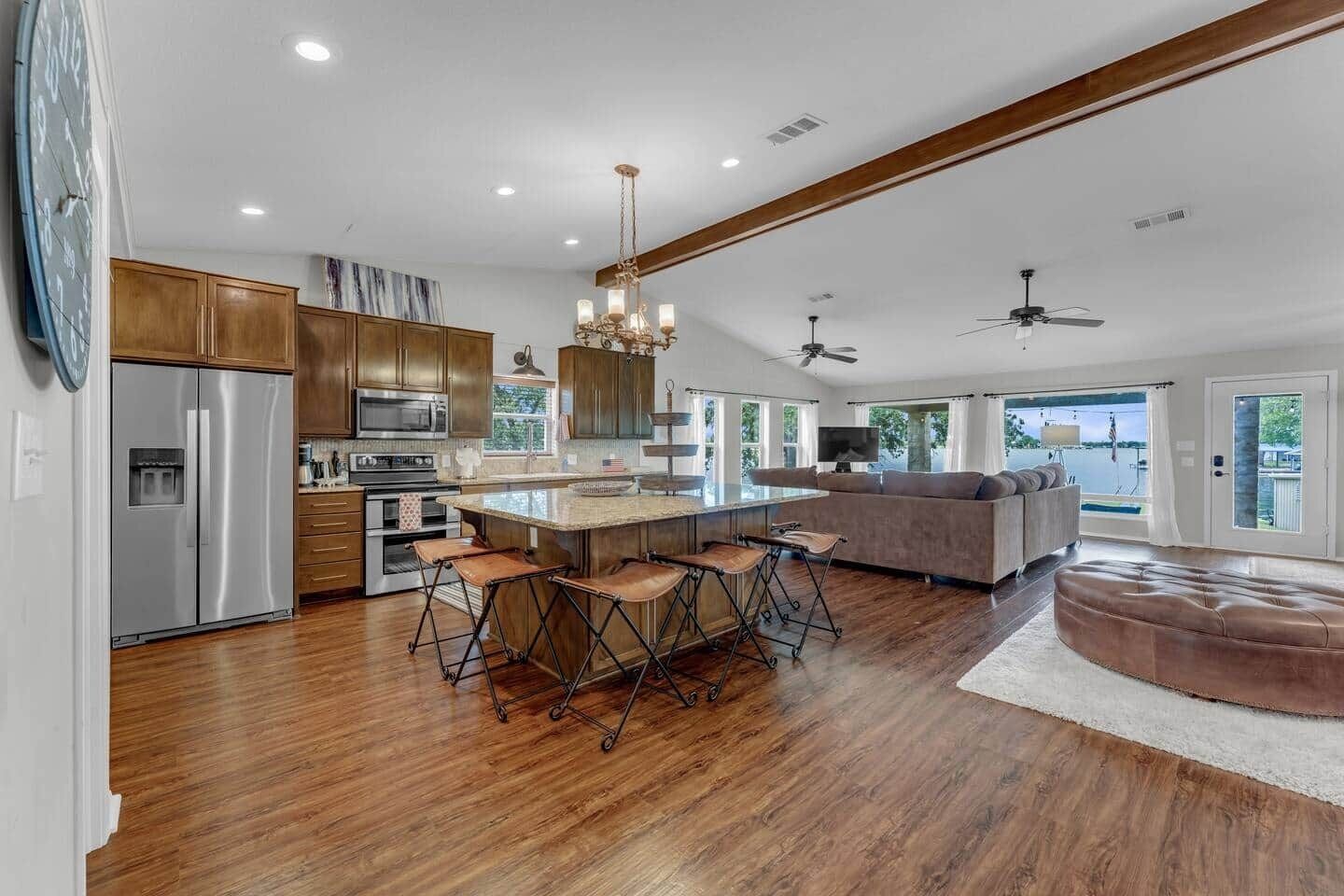 A spacious kitchen with a central island, bar stools, and a large window overlooking a body of water.