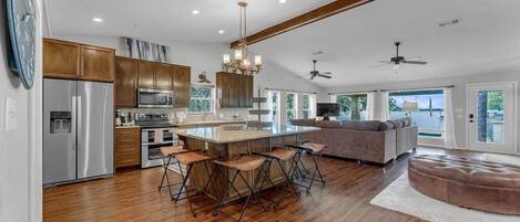 A spacious kitchen with a central island, bar stools, and a large window overlooking a body of water.