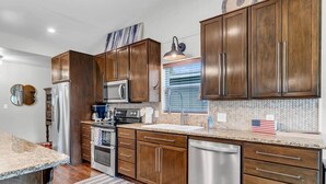 A modern kitchen with wooden cabinets, stainless steel appliances, and a striped rug. - Sunrise Siesta on Lake LBJ! (Sunrise Beach Village)