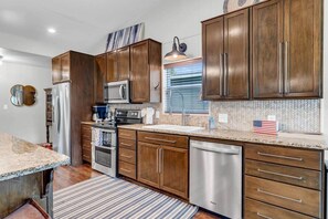 A modern kitchen with wooden cabinets, stainless steel appliances, and a striped rug. - Sunrise Siesta on Lake LBJ! (Sunrise Beach Village)