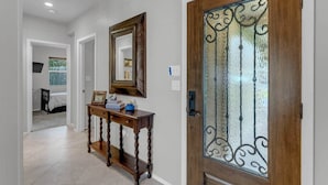 A hallway with a wooden console table, a mirror, and a door with decorative glass panels. - Sunrise Siesta on Lake LBJ! (Sunrise Beach Village)