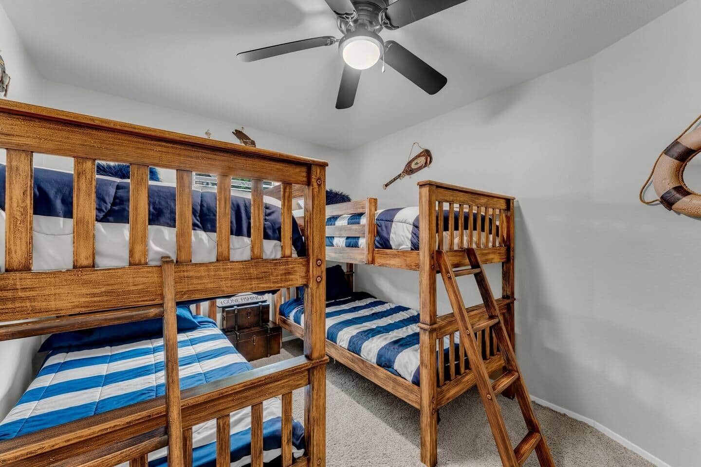Une chambre avec des lits superposés, un ventilateur de plafond et une petite commode.