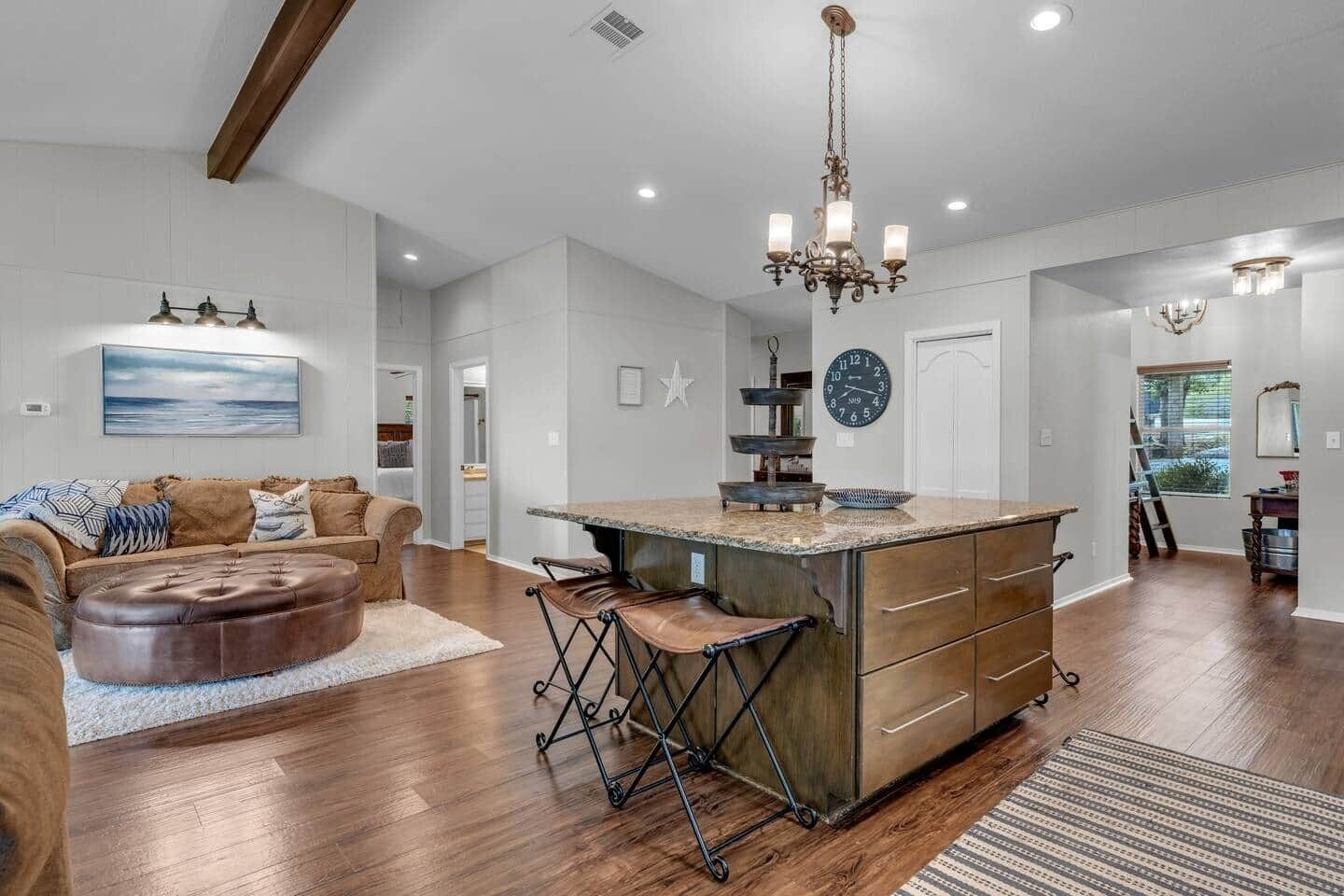 A spacious kitchen with a central island, wooden flooring, and a chandelier.