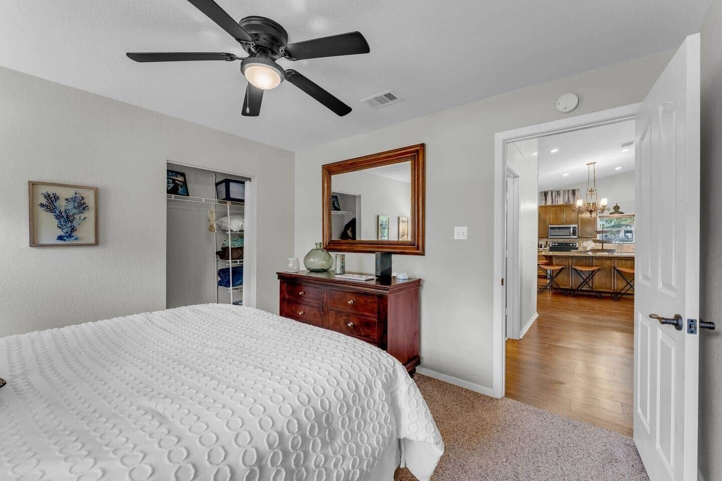 A bedroom with a bed, a dresser, a ceiling fan, a mirror, and a closet.
