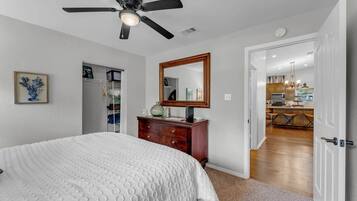 A bedroom with a bed, a dresser, a ceiling fan, a mirror, and a closet.