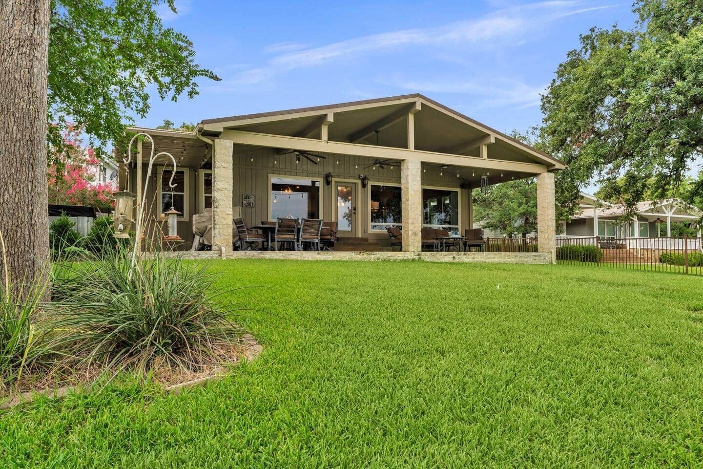 A covered outdoor seating area with tables and chairs, surrounded by a well-maintained lawn and trees.
