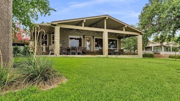 A covered outdoor seating area with tables and chairs, surrounded by a well-maintained lawn and trees.