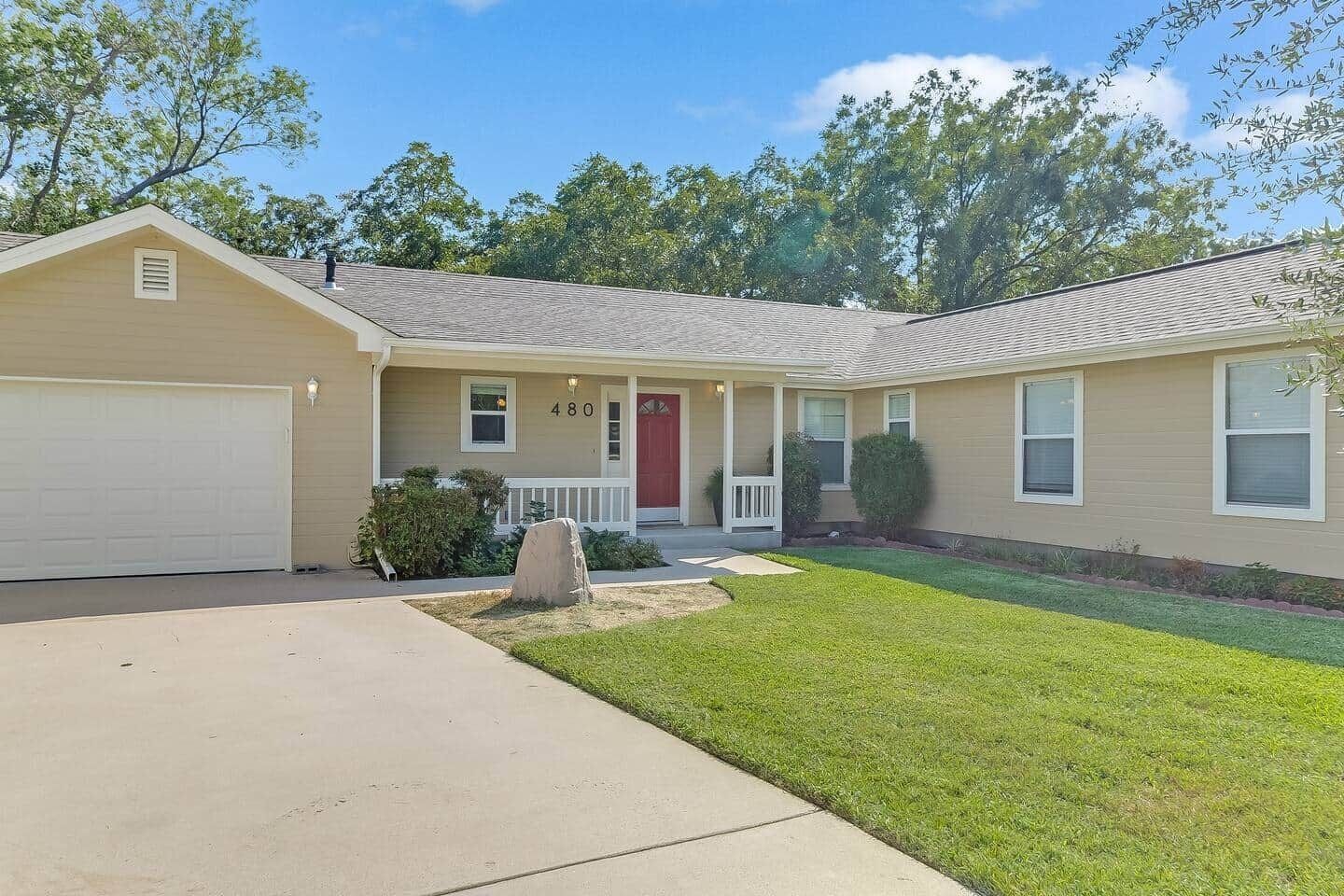 A single-story house with a red front door, a garage, and a well-maintained lawn.