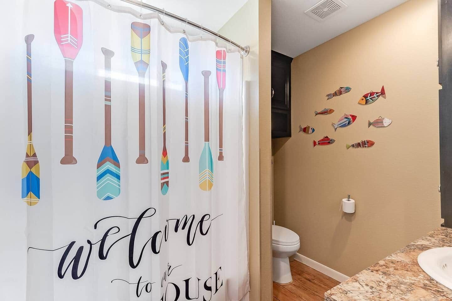A bathroom with a shower curtain featuring paddleboard designs and a wall with fish decals.