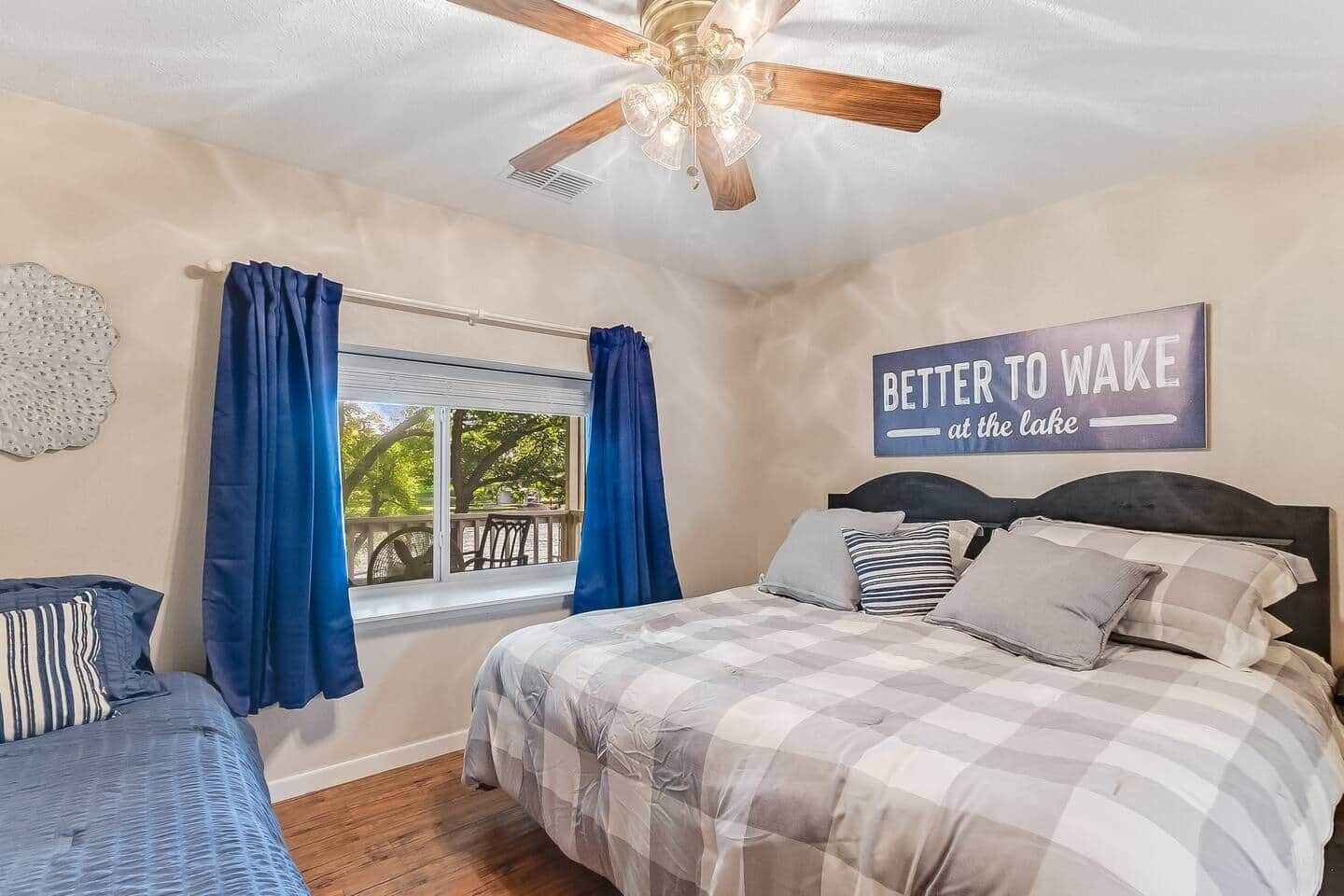 A bedroom with a bed, a window with curtains, a ceiling fan, and a motivational quote on the wall.