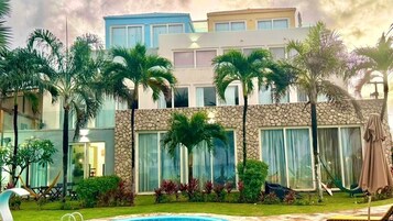 Un hotel de varios pisos con piscina, palmeras y fachada de piedra.