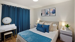 Ein Schlafzimmer mit einem Bett, Nachttischen, einem Schminktisch mit Spiegel und Kunstwerken an der Wand.