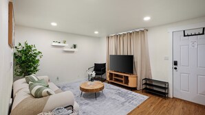 Ein Wohnzimmer mit einer Couch, einem Fernseher, einer Holz-Unterhaltungseinheit und einer Tür.