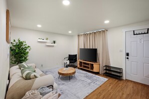 Sala de estar com sofá, televisão, aparador de madeira e uma porta.