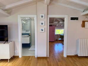 Ein Zimmer mit Holzboden, einem Fernseher, einem Badezimmer mit Spiegel, Waschbecken und einem pinken Kühlschrank.