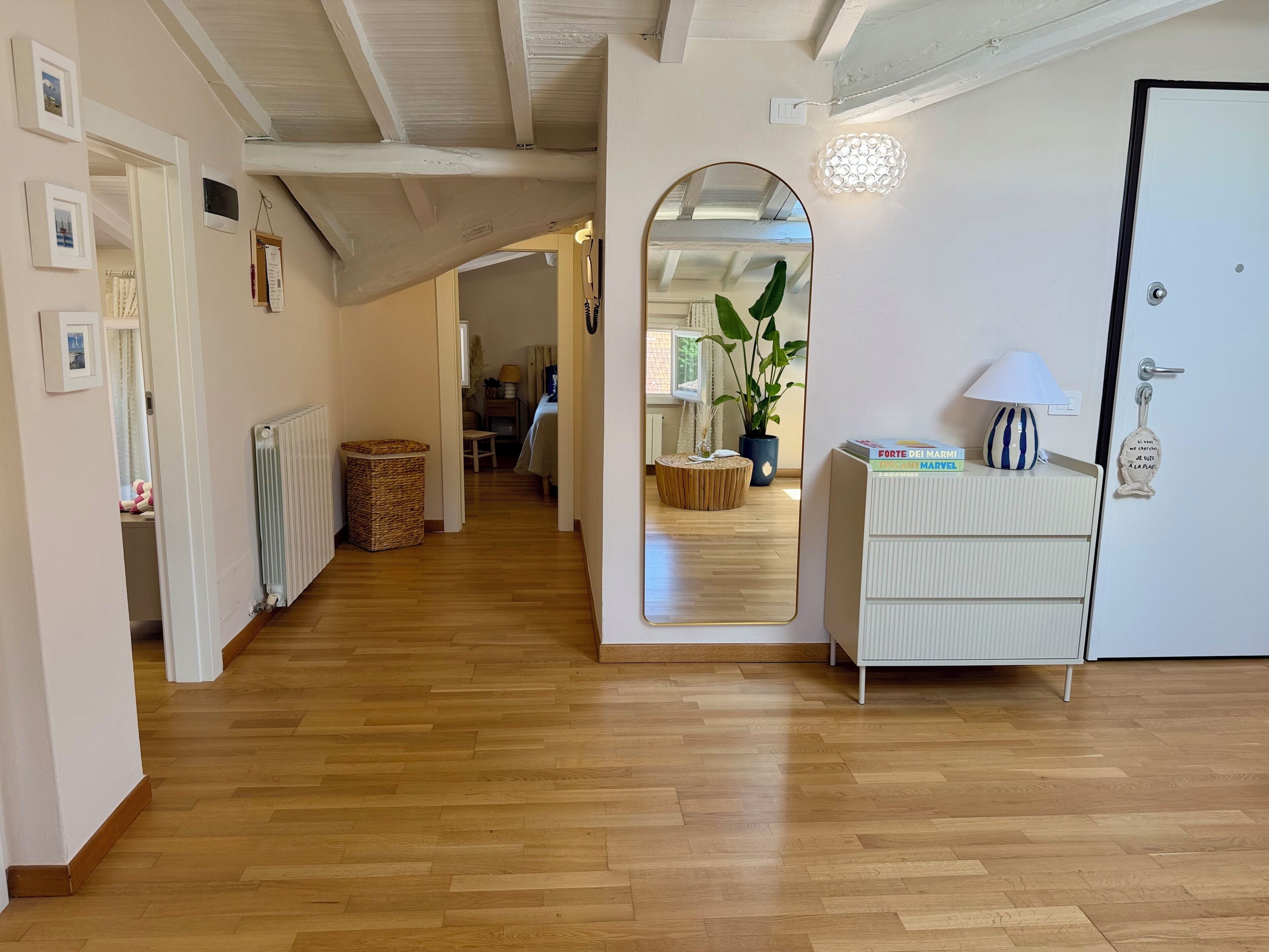 Un couloir doté d’un plancher en bois, d’une commode blanche, d’un miroir et d’une porte ornée d’une poignée décorative.
