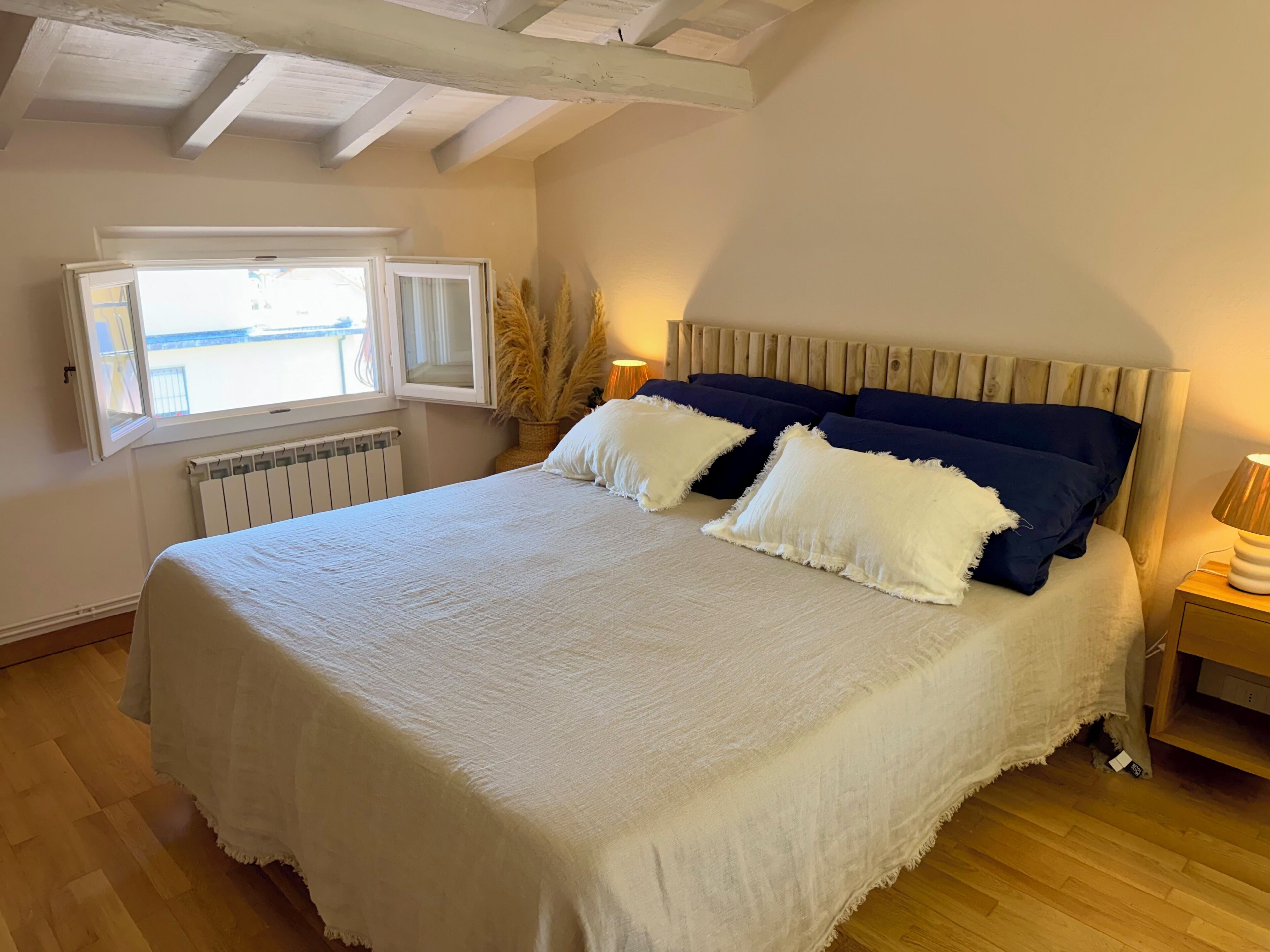 Un dormitorio con cama, ventana, radiador y mesita de noche.