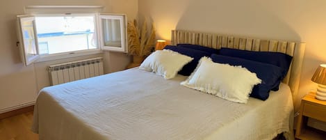Un dormitorio con cama, ventana, radiador y mesita de noche.